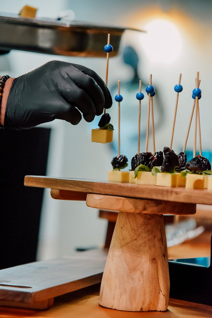 A gloved hand carefully arranging gourmet appetizers on skewers at a restaurant.